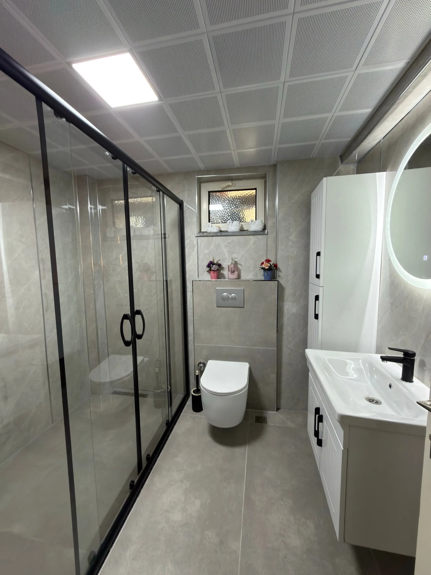 Siyah çerçeveli duşakabin ve mermer görünümlü duvarlarla yenilenmiş banyo