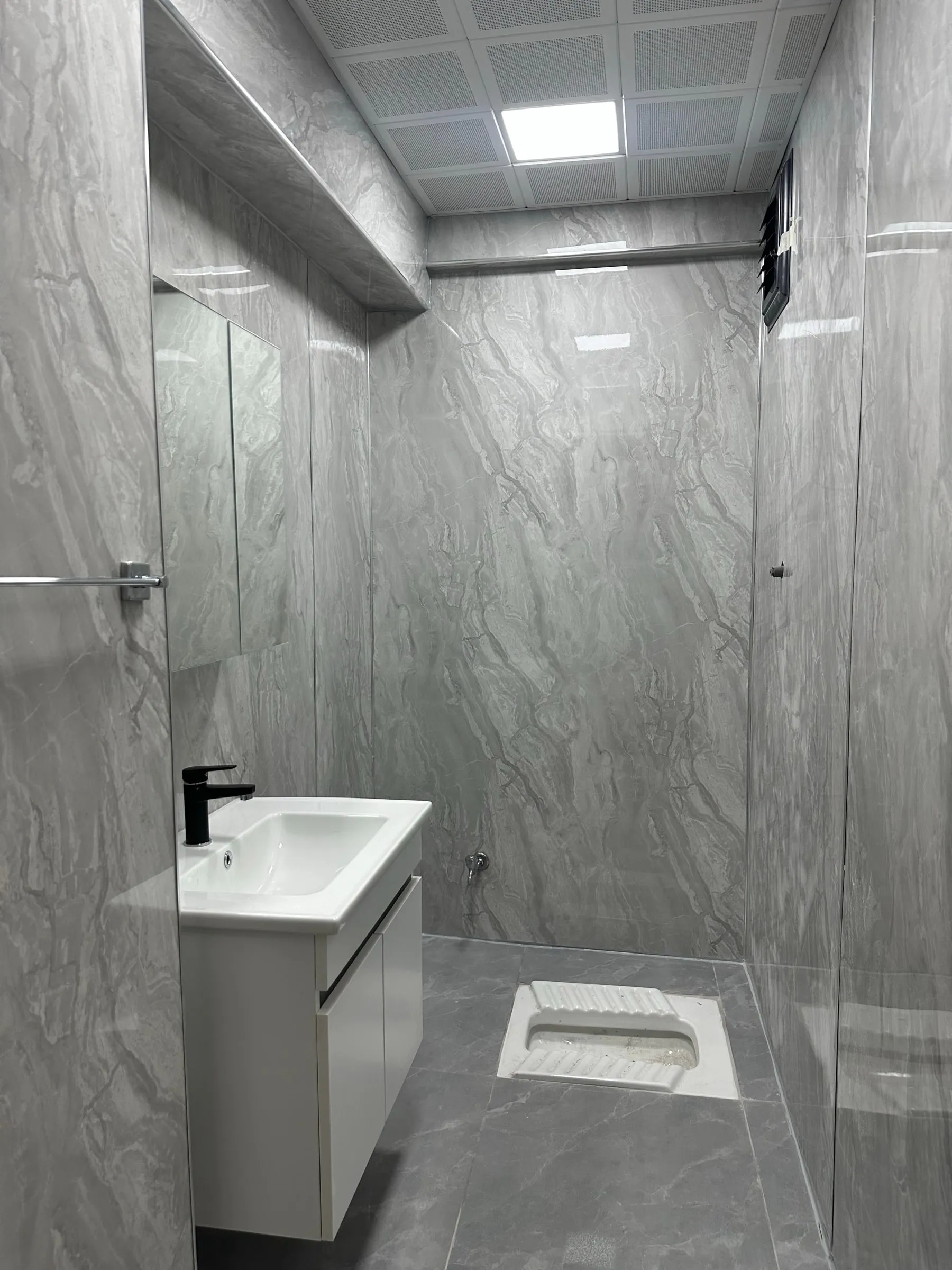 Duvarları gri PVC mermer plaka ile kaplanmış, derzsiz küçük tuvalet